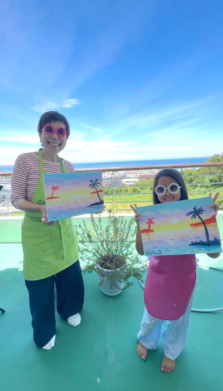 Two Pinto Beetle guests holding tropical sunset paintings on the ocean-view terrace