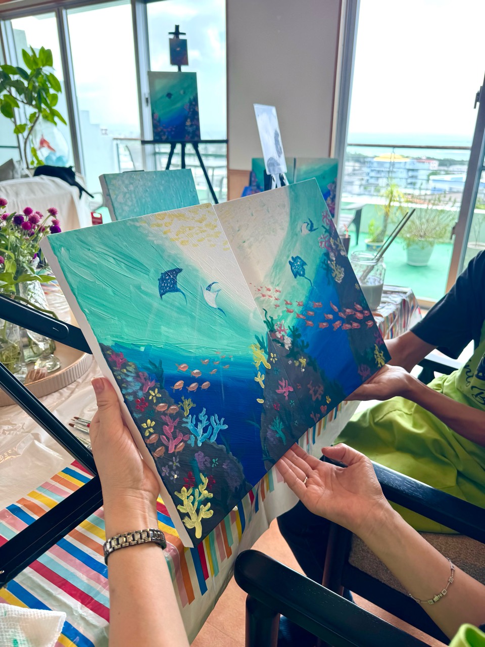Pinto Beetle guests holding finished Under the Sea pair paintings with coral, fish, and manta rays